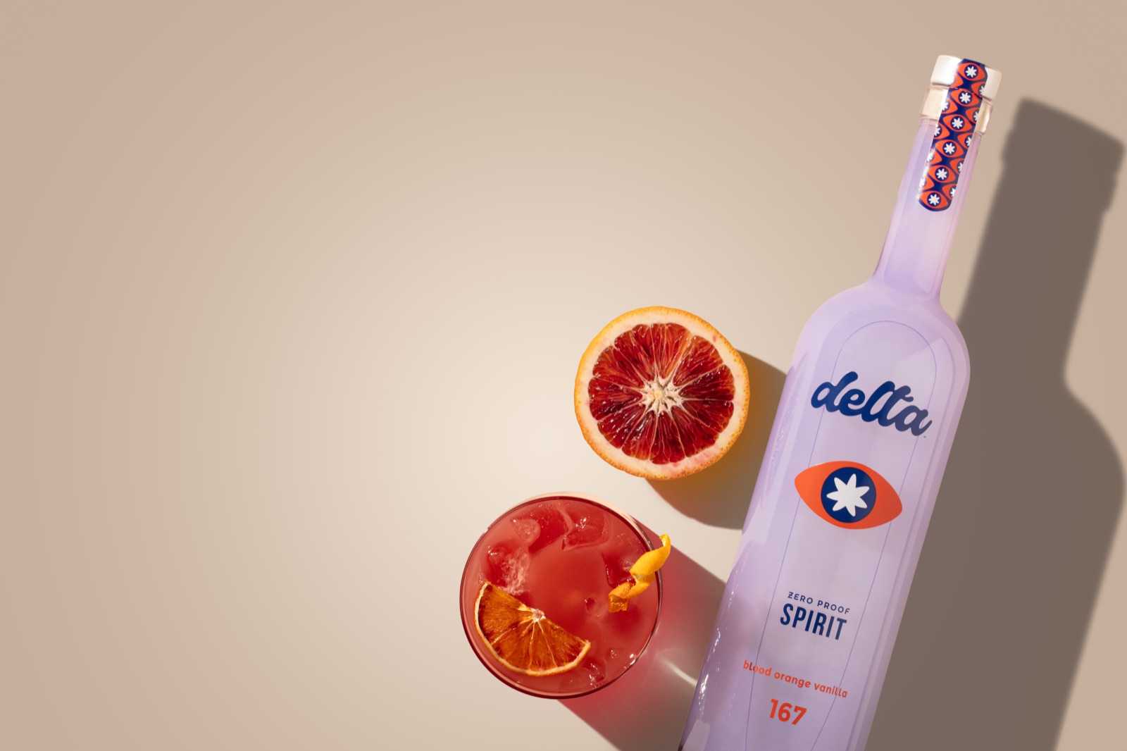 A blood orange cocktail in a rocks glass over ice with citrus twist garnish, alongside the Spirit bottle.
